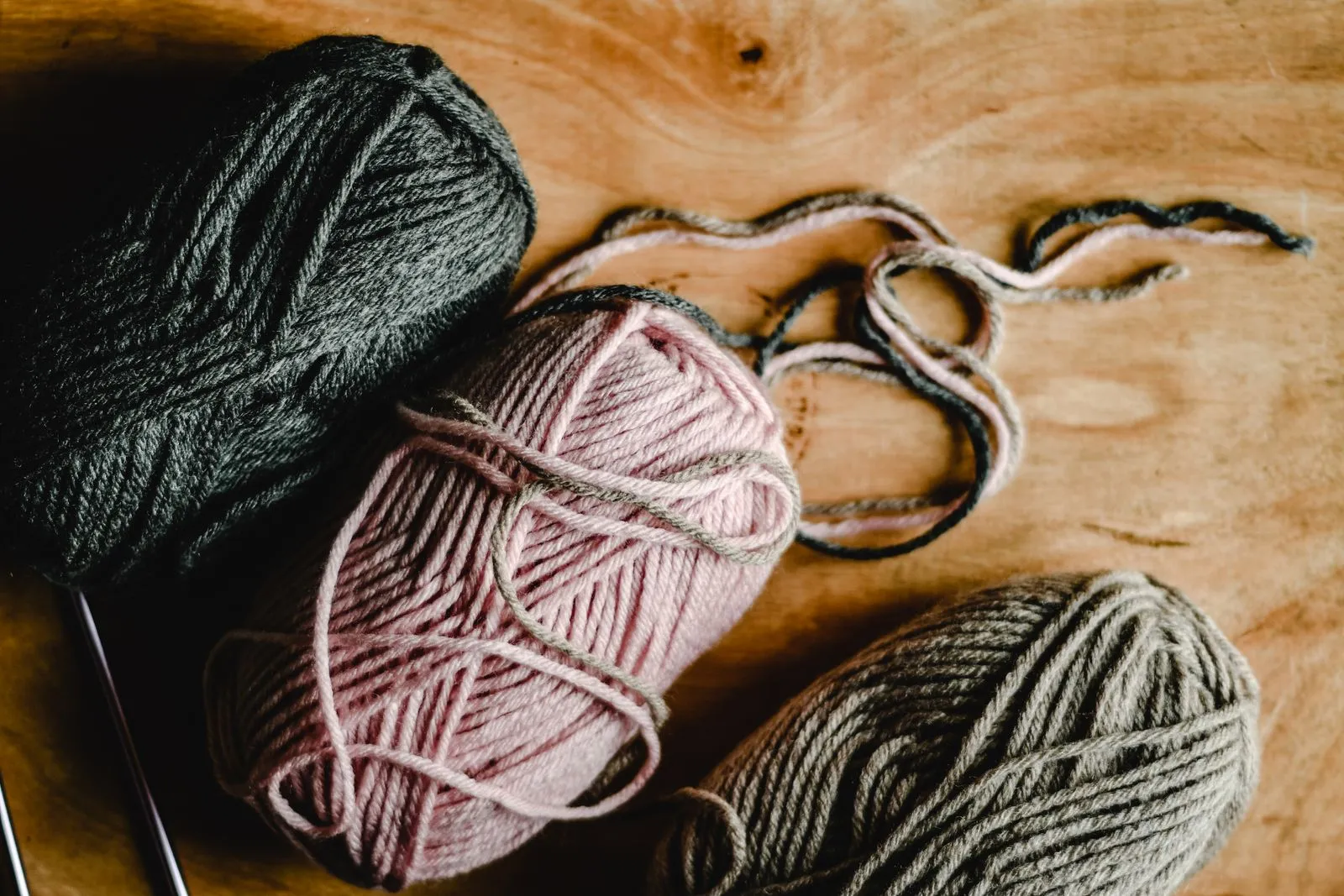 Close-up of three yarn balls in different colors on a wooden surface, showcasing textures and craft materials.